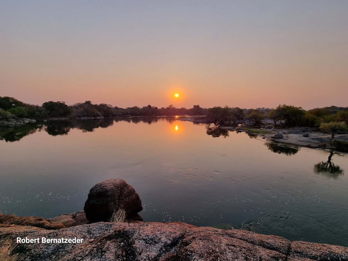 Sunset over a calm river with rocks in the foreground