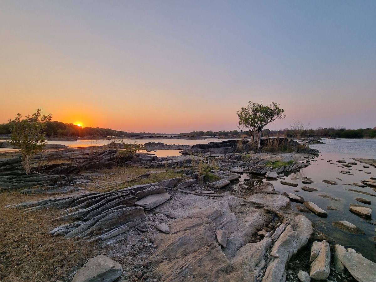A rocky river landscape at sunset with a lone tree on the bank