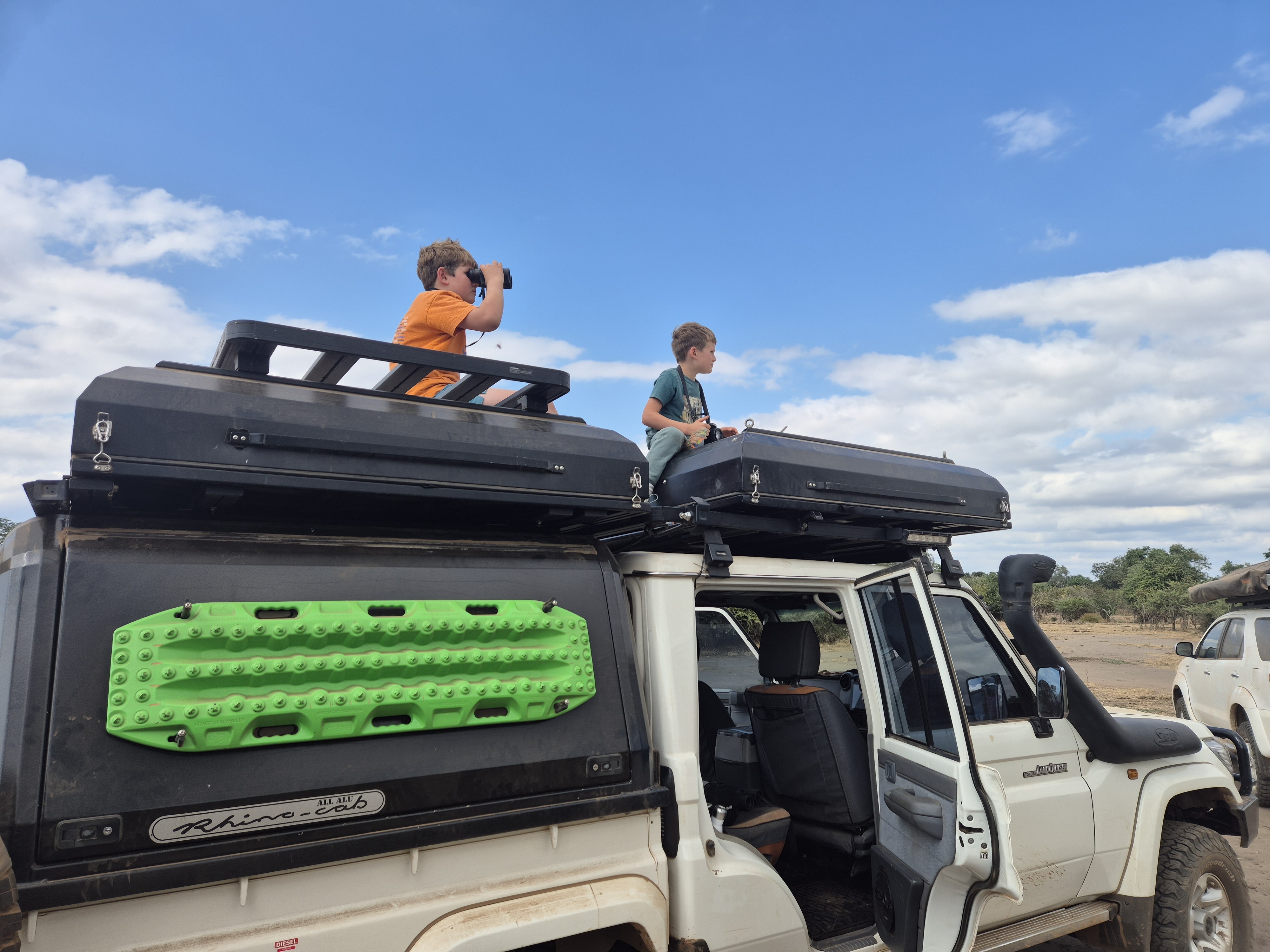 Two boys sitting on rooftop tents, looking out over the savanna